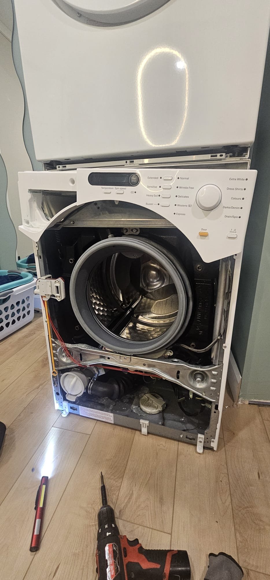 Bosch front-load stacked washing machine with front panel removed exposing drum, gasket, and drain pump area for leak repair by Caspian Hamilton
