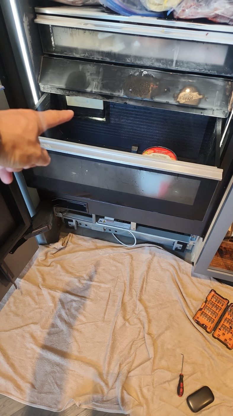 Bottom-mount freezer drawer pulled out during repair, technician pointing to the fault, by Caspian Appliance Repair in Hamilton, Ontario