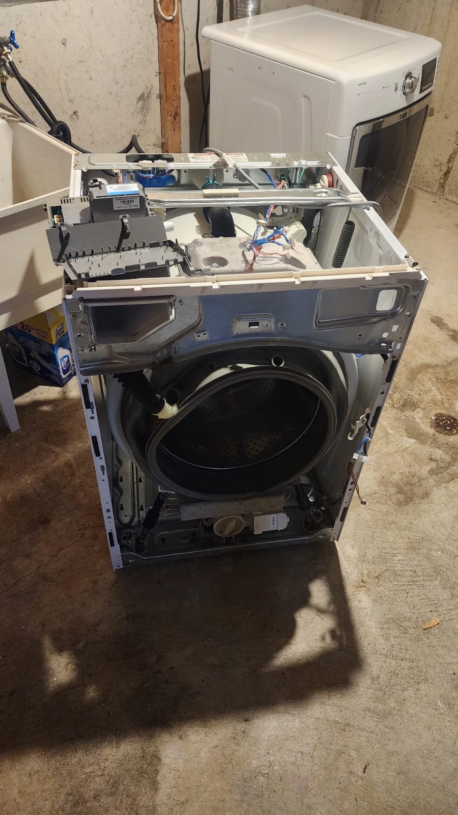 Whirlpool front-load washing machine fully disassembled in basement laundry showing control board and motor for electronic diagnostics by Caspian Appliance Repair Hamilton