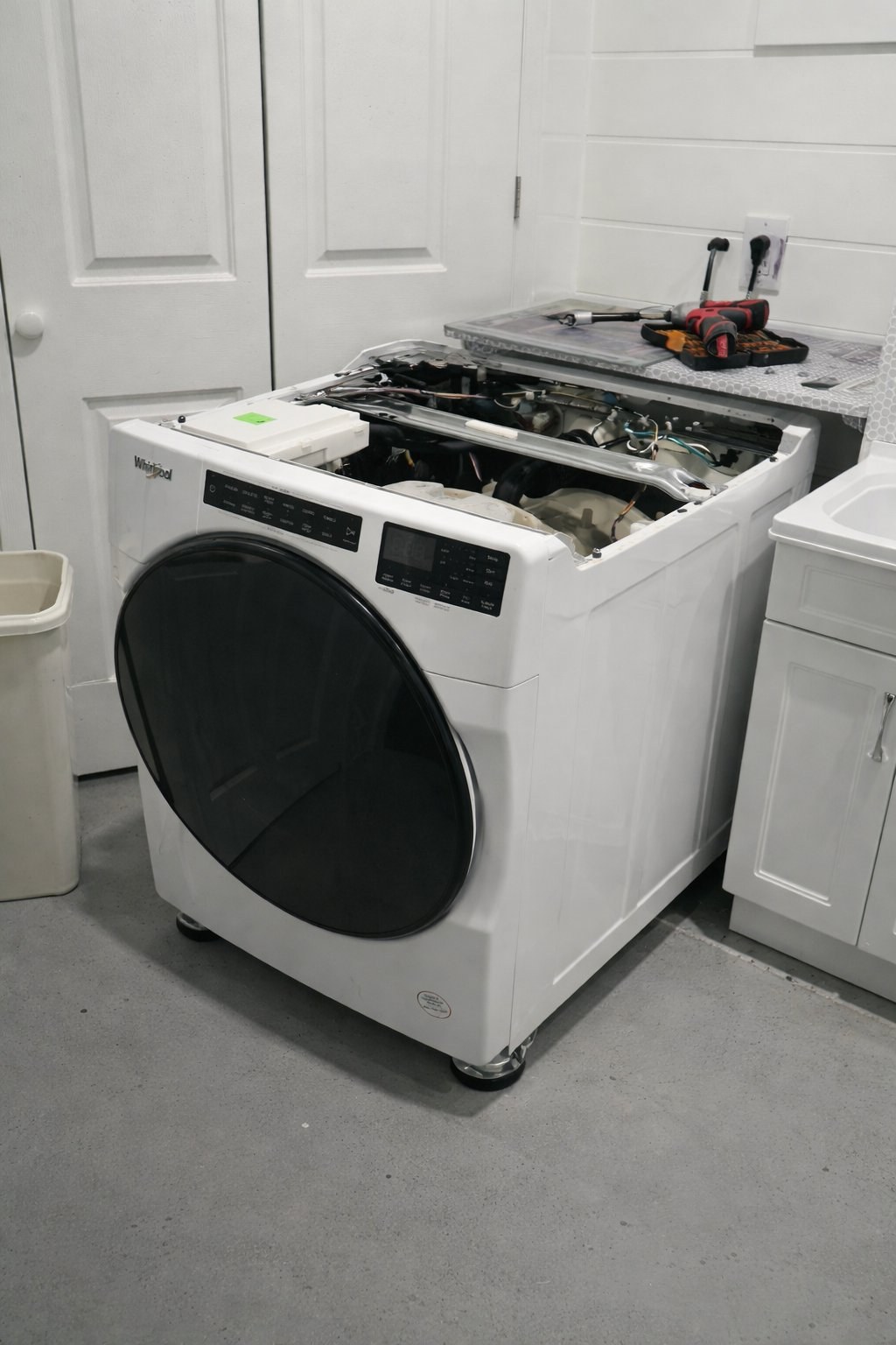 Whirlpool front-load washing machine with top panel removed for repair service in a Hamilton, Ontario laundry room by Caspian Appliance Repair